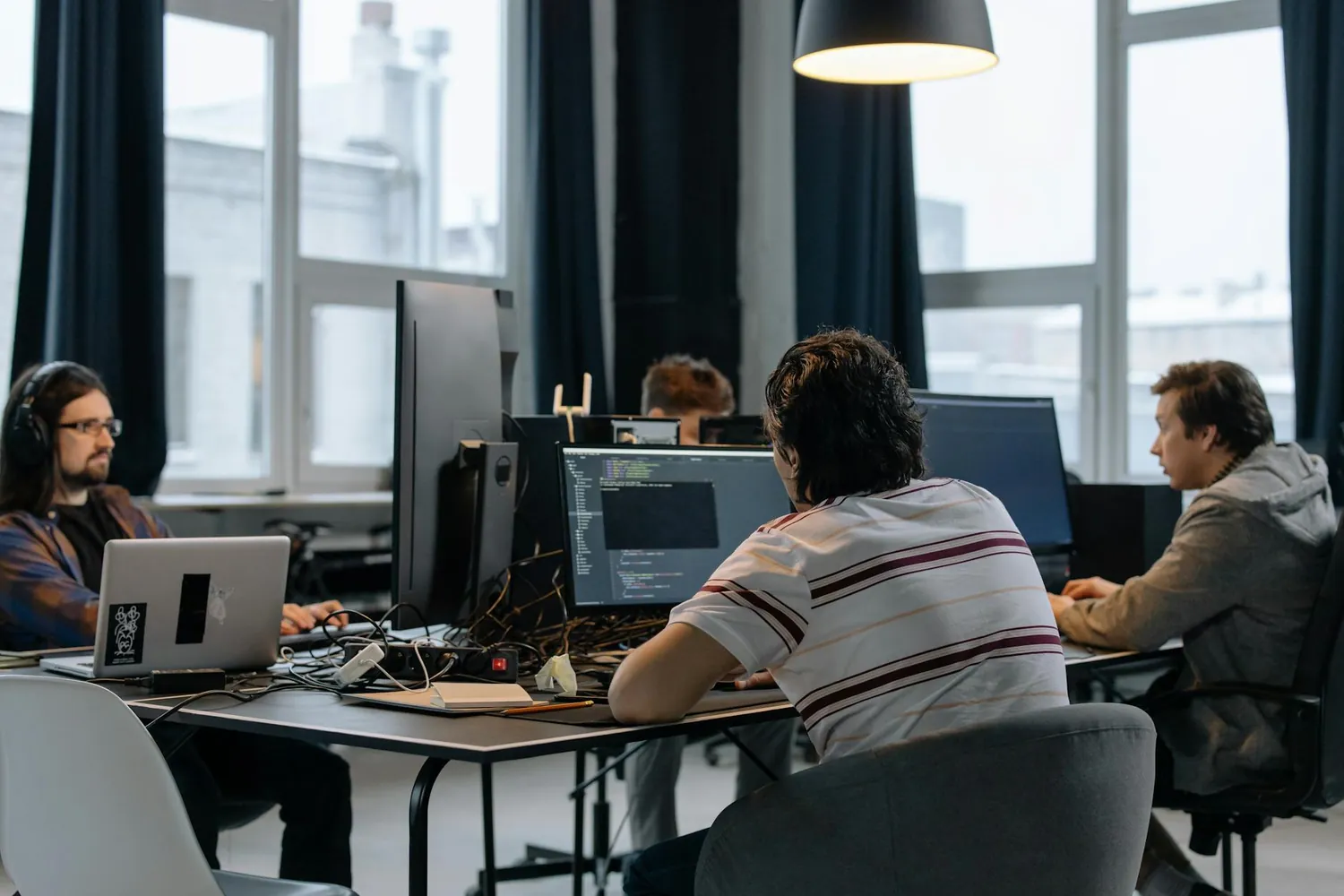 Several colleagues working at desks with monitors in an open-plan office, seen from behind