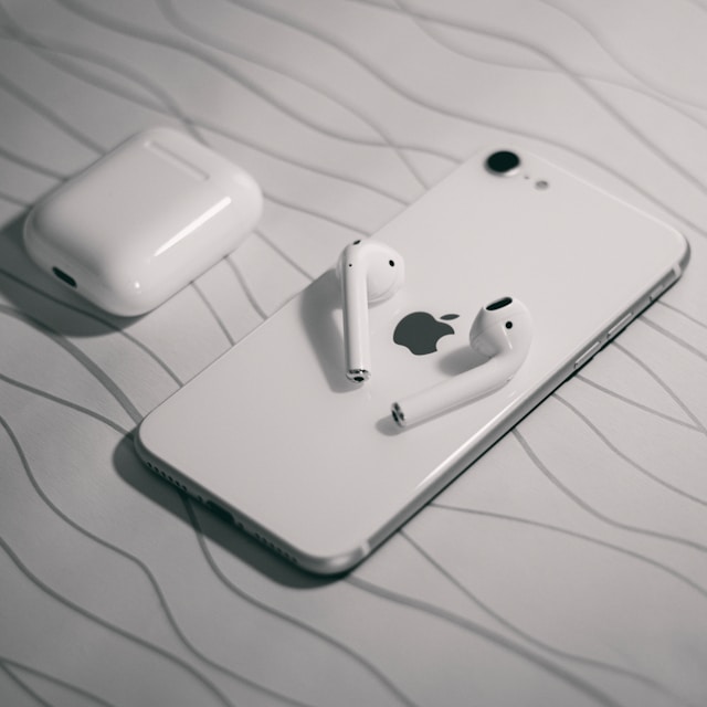 A pair of white wireless earbuds and a white smartphone lying on a pale surface
