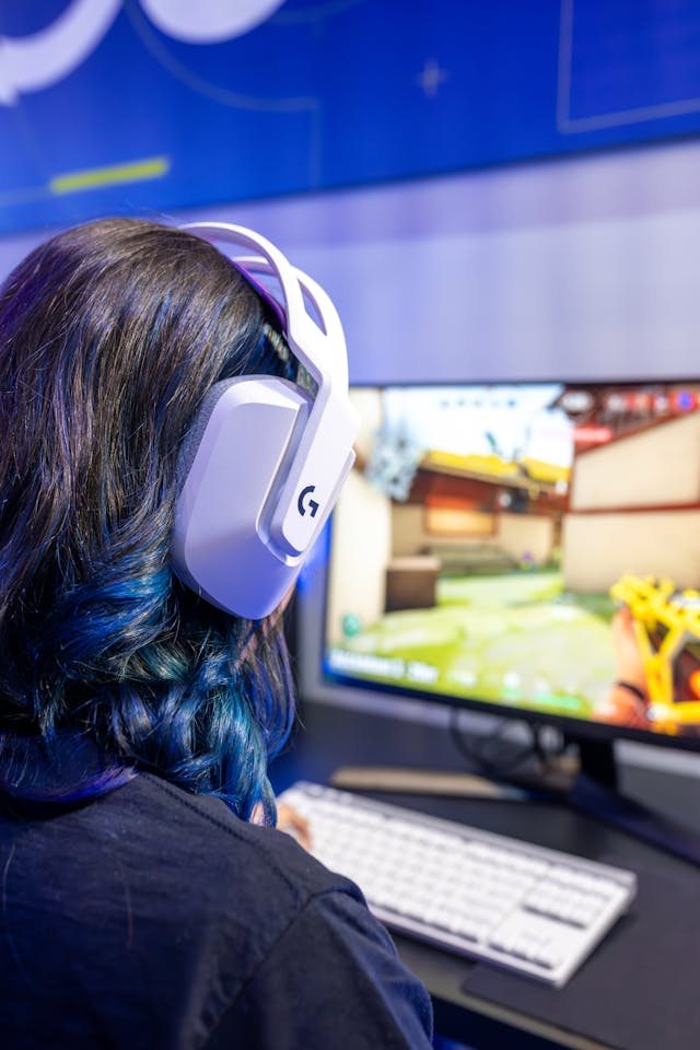 A person wearing a white gaming headset in front of a monitor showing a game