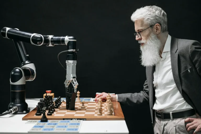 An older man in a suit playing chess against a robotic arm across a board