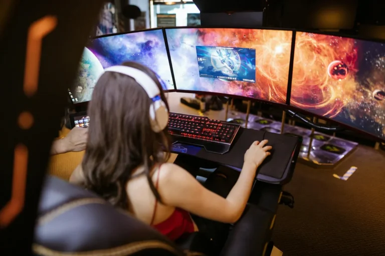 A person wearing headphones at a desk with three monitors showing colourful space imagery
