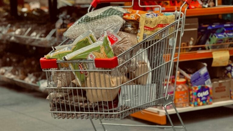 A metal shopping cart loaded with groceries standing in a supermarket aisle