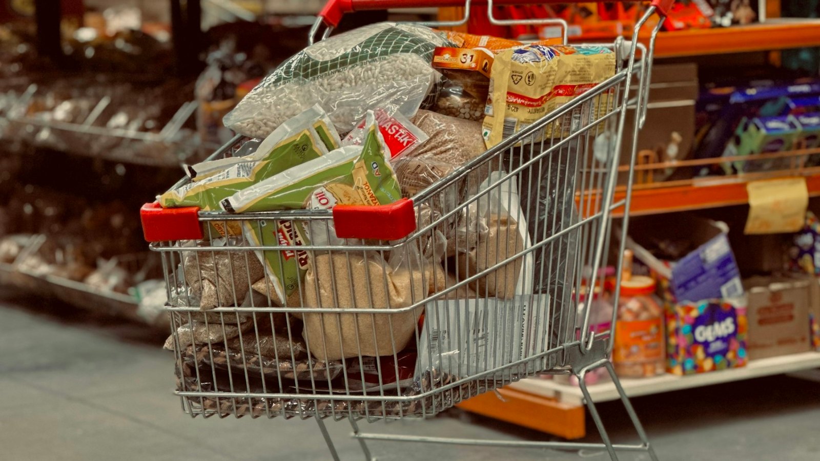 A metal shopping cart loaded with groceries standing in a supermarket aisle