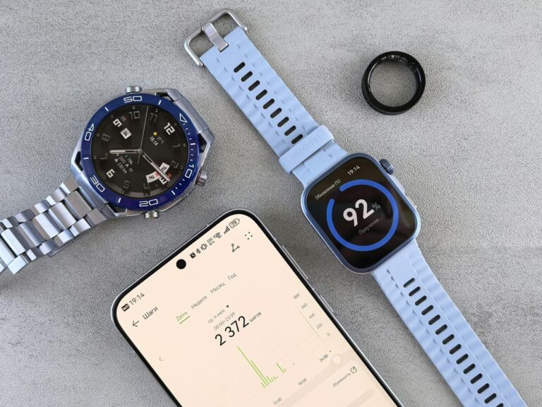 Two smartwatches, a smart ring and a phone laid out on a grey surface