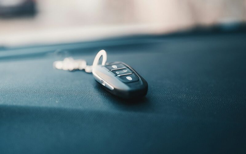 A car key fob lies on a dark dashboard inside a vehicle