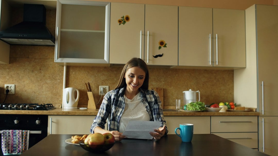 A smiling woman reads a printed document at her kitchen table