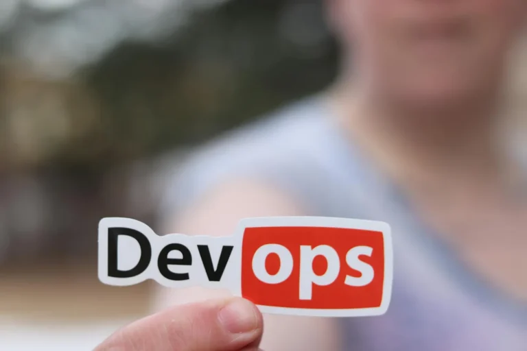 A sticker reading DevOps held up in front of a blurred background