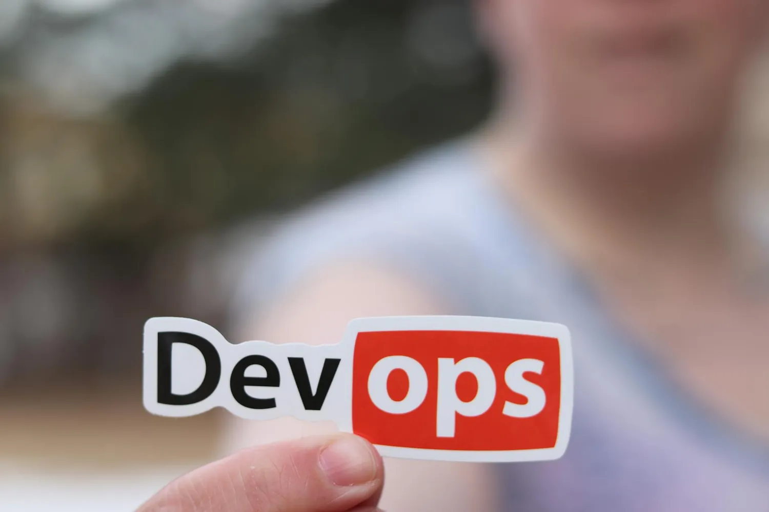 A sticker reading DevOps held up in front of a blurred background