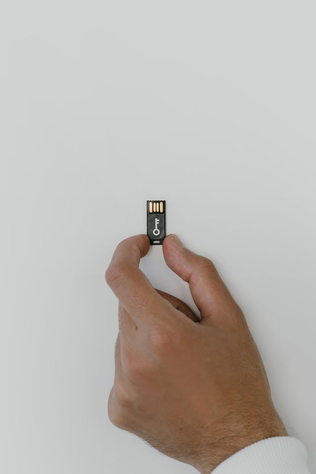 Two hands holding a small black USB security key against a plain background