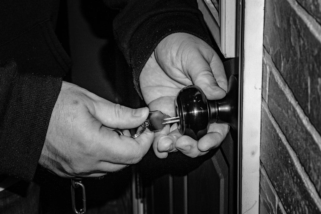 Close-up black and white image of hands picking the lock on a door knob.