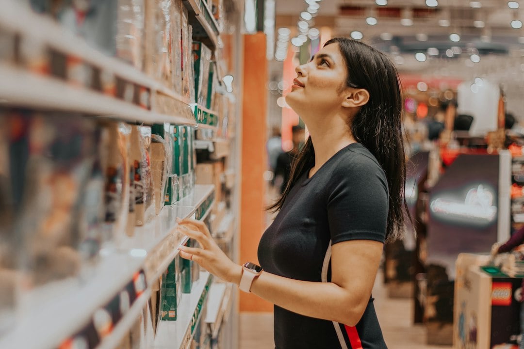 A shopper looks up at stocked retail shelves while reaching for a packaged item in a store aisle