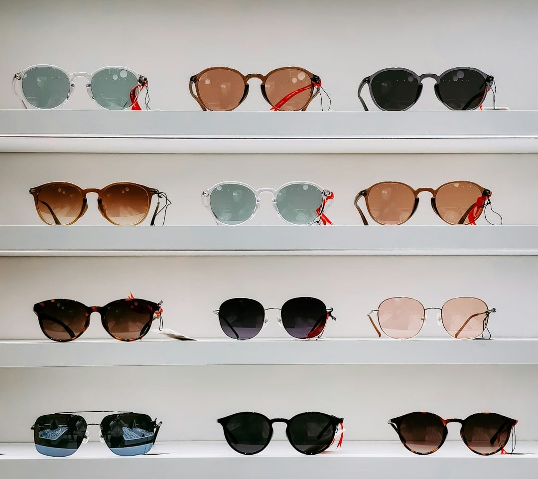 Twelve pairs of sunglasses with red tags lined up on white display shelves