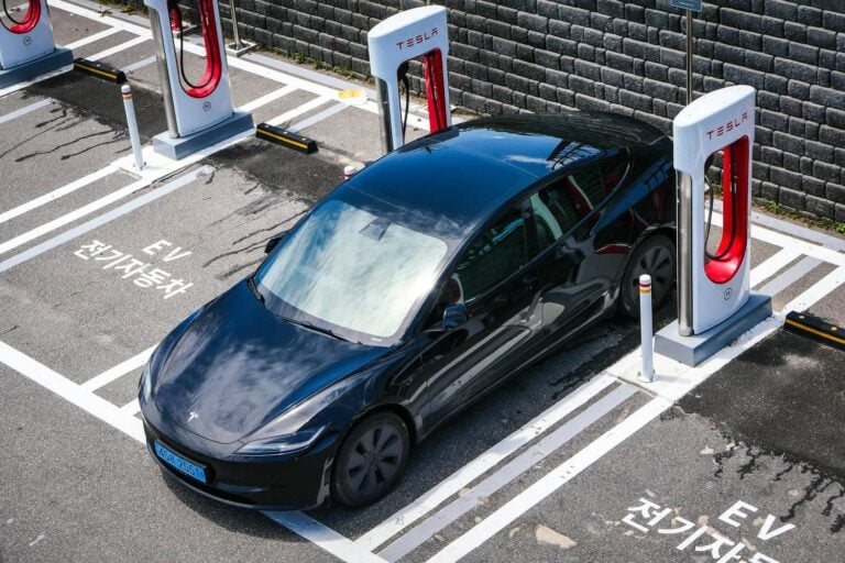 A dark electric car parked at a row of charging stations in a marked bay