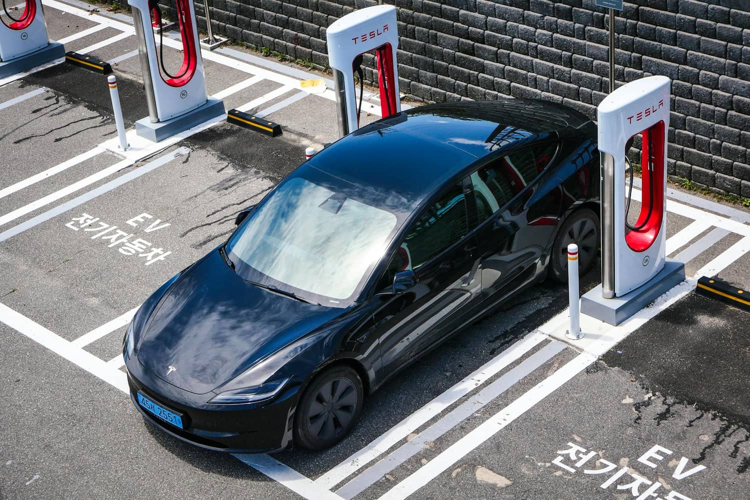 A dark electric car parked at a row of charging stations in a marked bay